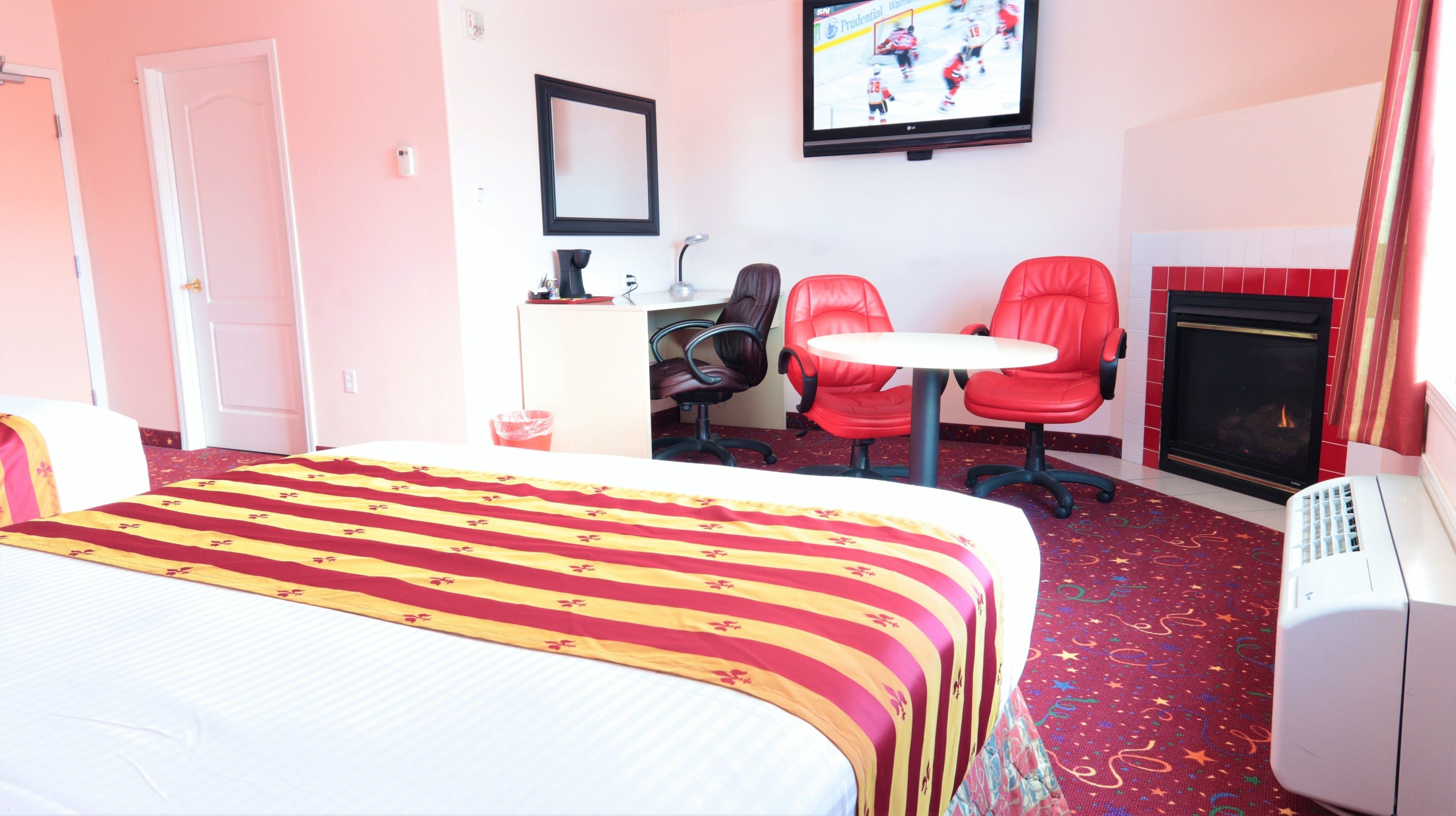 Une chambre d’hôtel avec un grand lit, un bureau avec deux chaises rouges, une télévision et une cheminée.