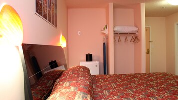 A bedroom with a bed, a bedside table, a hanging light, a closet with a hanging shelf, and a door.