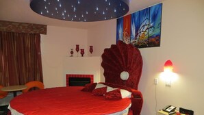 A large bed with a red headboard, a bedside table with a phone and a lamp, and a painting on the wall. - Crystal Star Inn Edmonton Airport (Leduc)