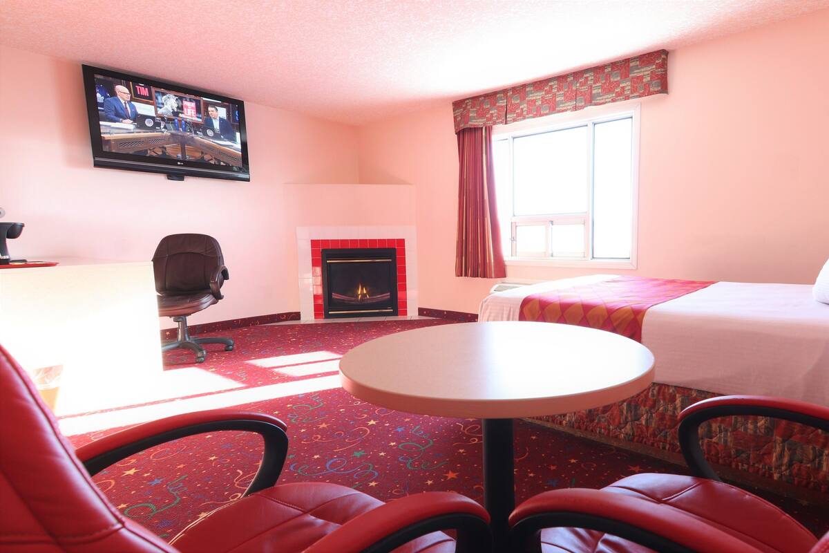 Una habitación de hotel con cama, escritorio con silla, televisor y chimenea.