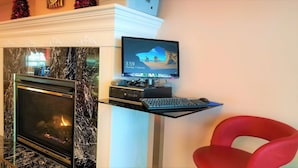 A modern living room with a fireplace, a mounted TV, a computer setup, and a red chair. - Crystal Star Inn Edmonton Airport (Leduc)