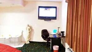 A hotel room with a bed, a desk with a computer, a TV, and a bathtub. - Crystal Star Inn Edmonton Airport (Leduc)