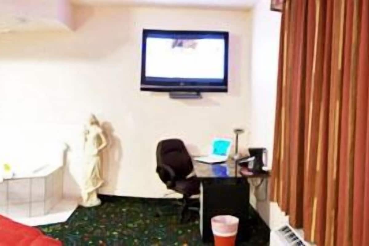 Una habitación de hotel con una cama, un escritorio con una computadora, un televisor y una bañera.