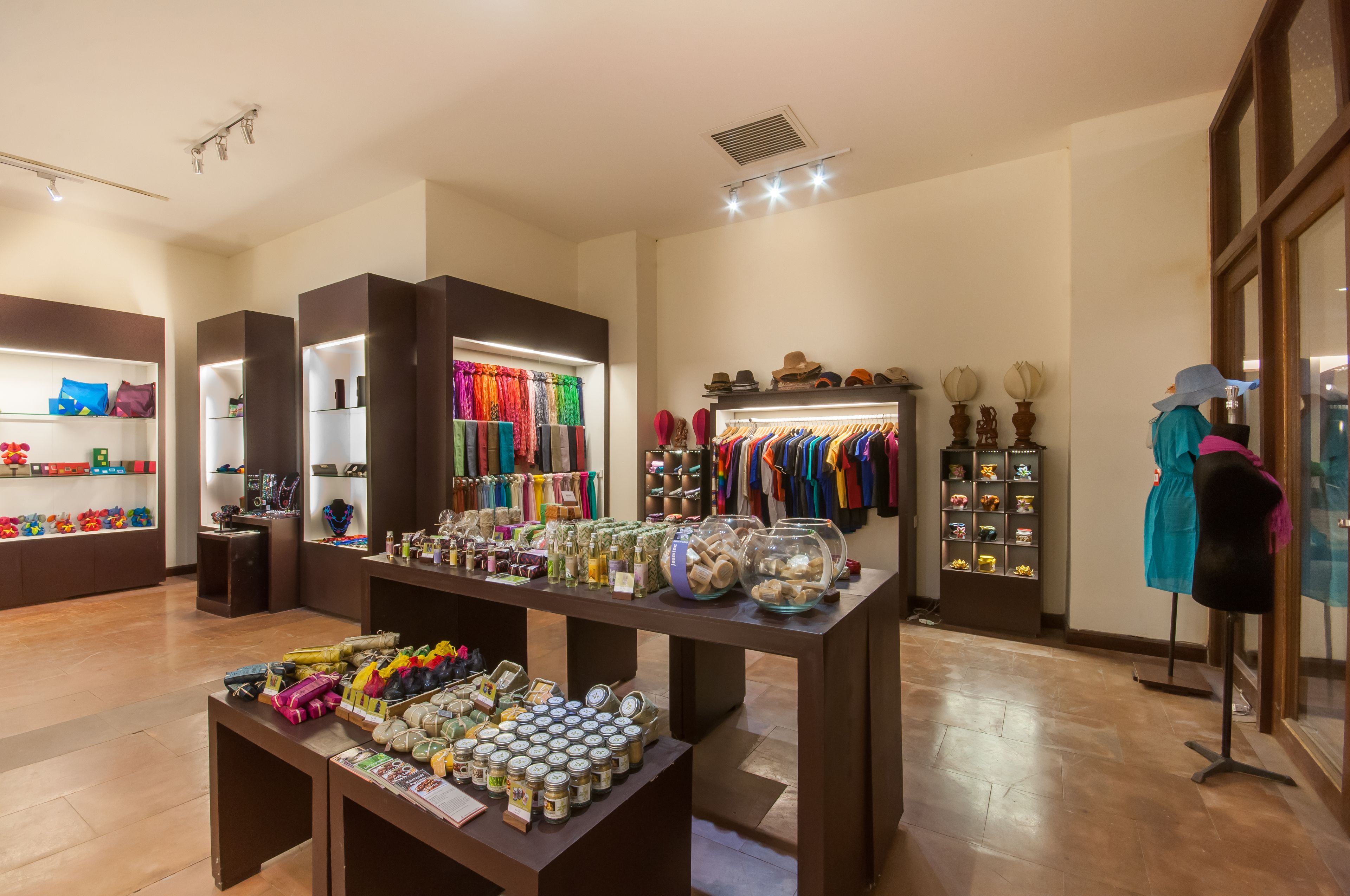 A boutique store with shelves of colorful scarves, a display of hats, and a mannequin dressed in a blue outfit.