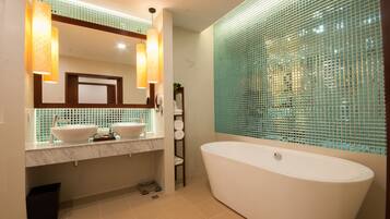 A modern bathroom with two sinks, a large bathtub, and a mirror with pendant lights.