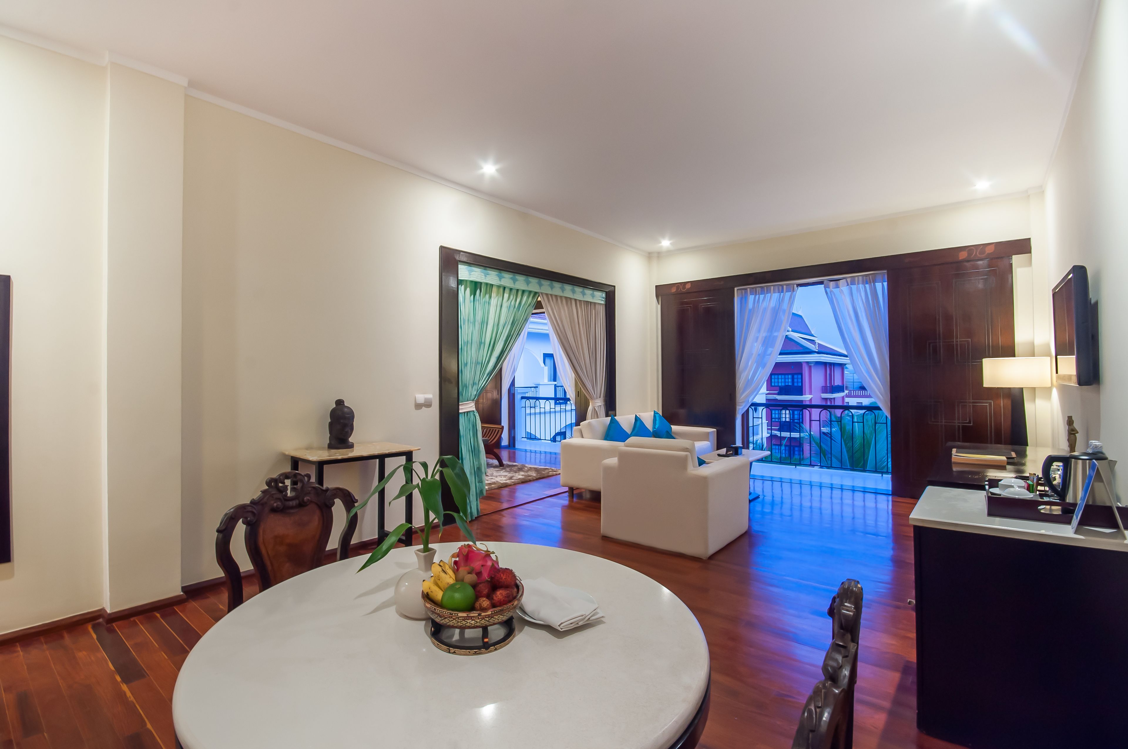 A spacious living room with a round dining table, a sofa set, and a view of a balcony.