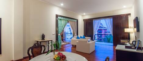 A spacious living room with a round dining table, a sofa set, and a view of a balcony.