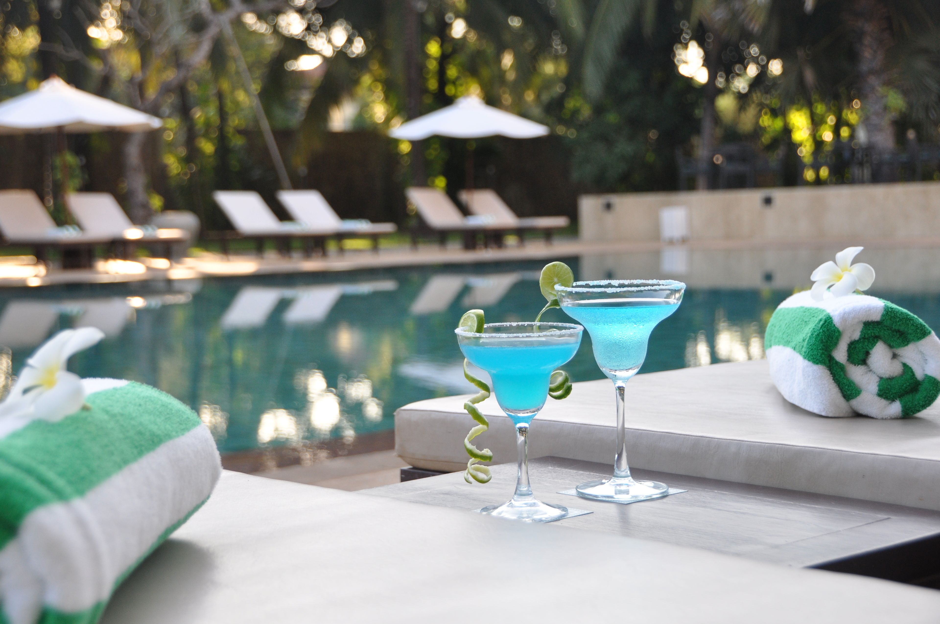 Área de piscina com espreguiçadeiras e dois cocktails sobre uma mesa.