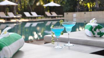 Área de piscina com espreguiçadeiras e dois cocktails sobre uma mesa.