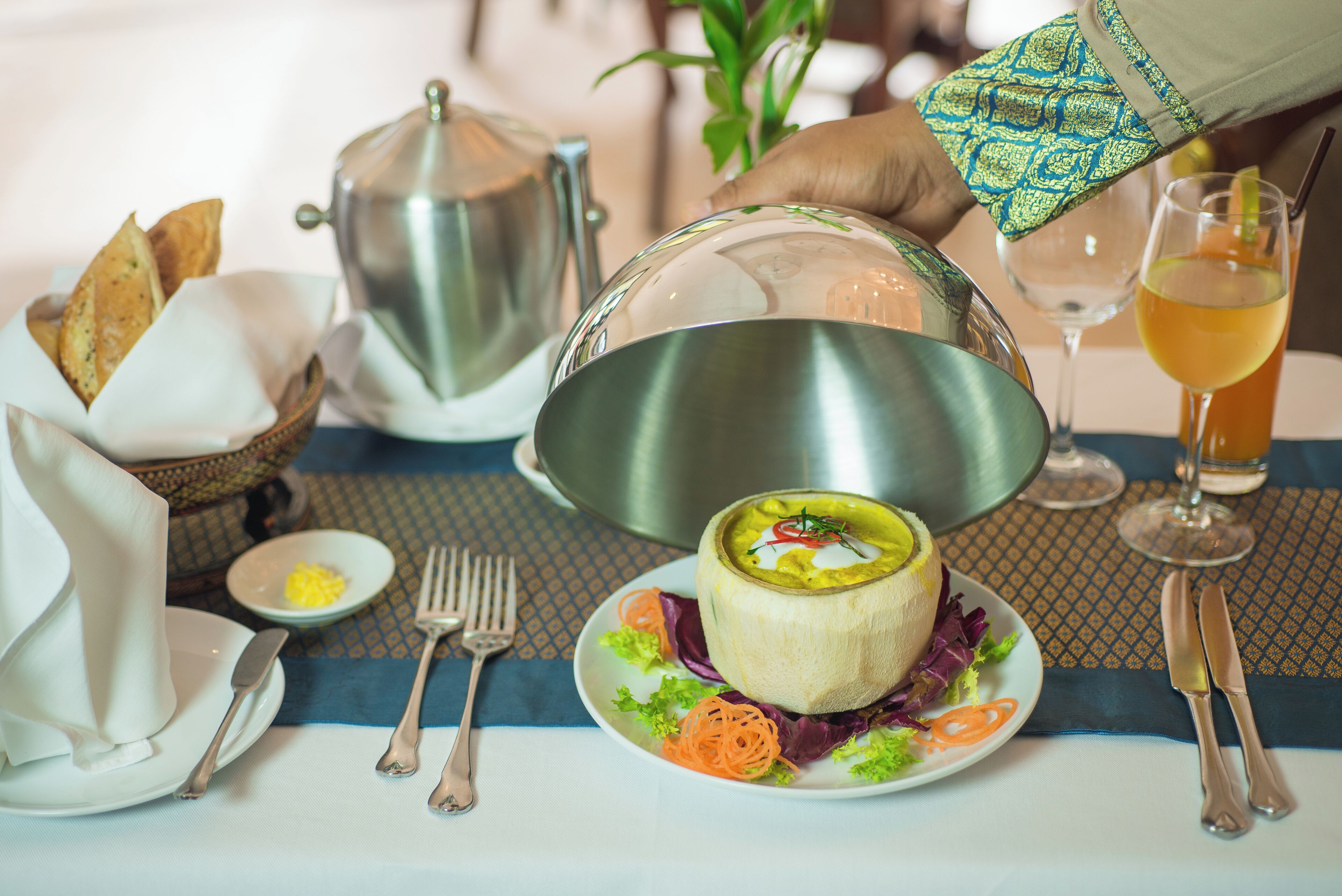 A dining table with a meal setup including a bowl of soup, a plate with vegetables, bread, and a glass of drink.