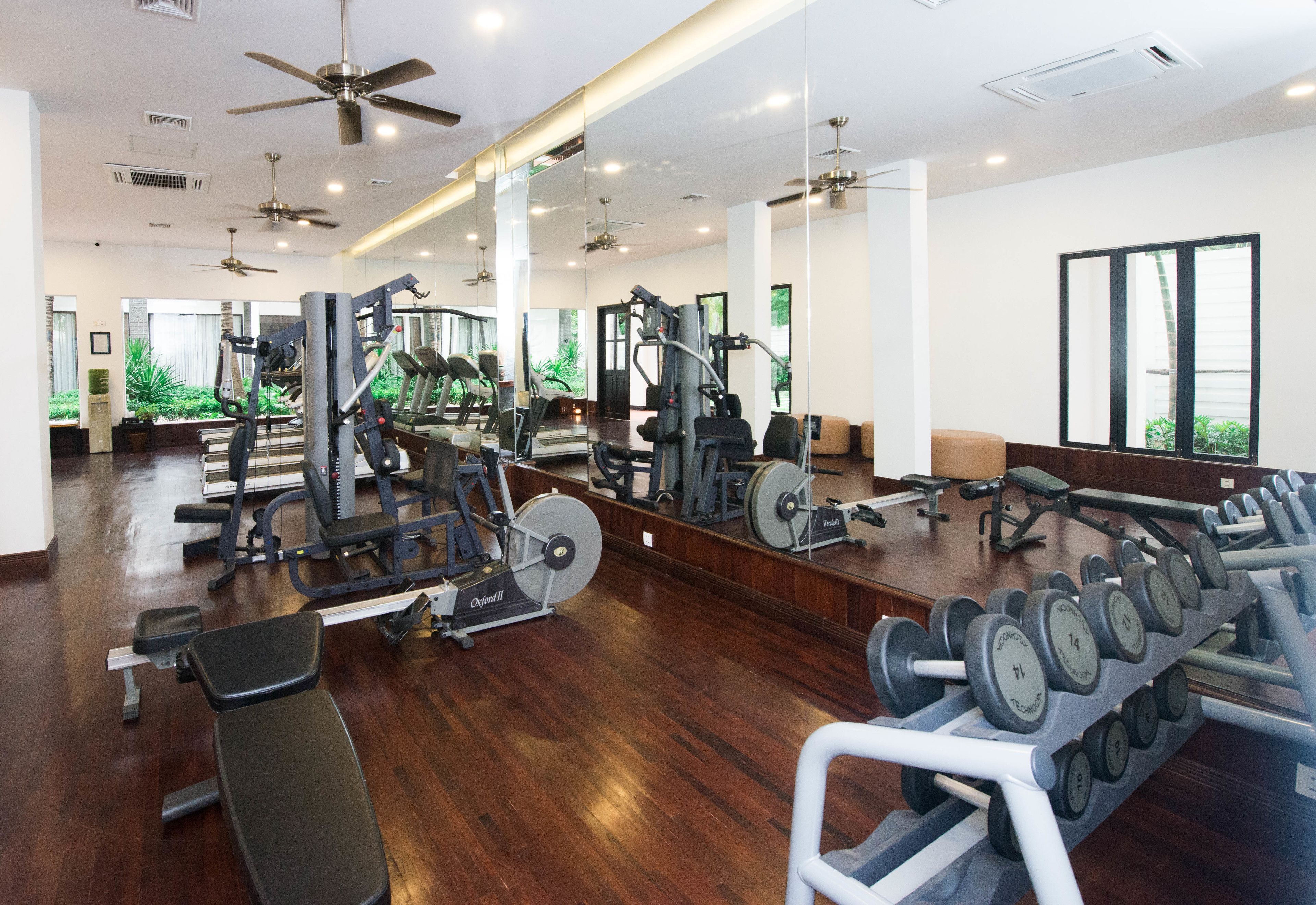 A spacious gym with various exercise equipment, large mirrors, and a wooden floor.