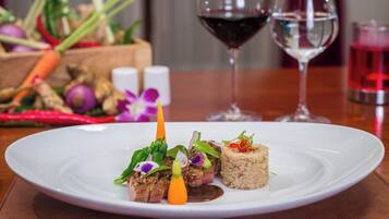 A white plate with a dish of meat, vegetables, and rice. There are two wine glasses in the background.