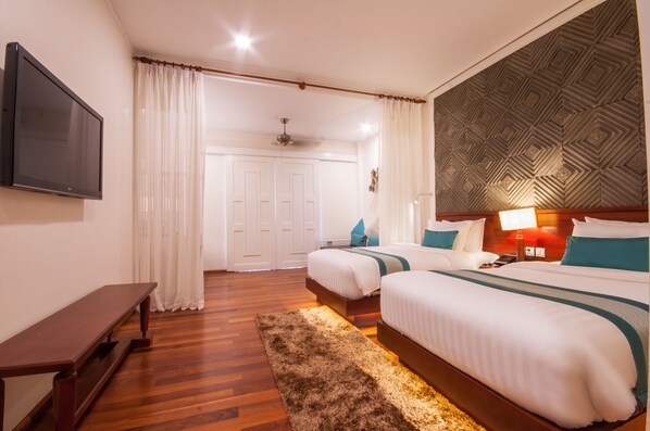 Une chambre d’hôtel avec deux lits, une télévision, un banc et un plafond décoré de motifs.