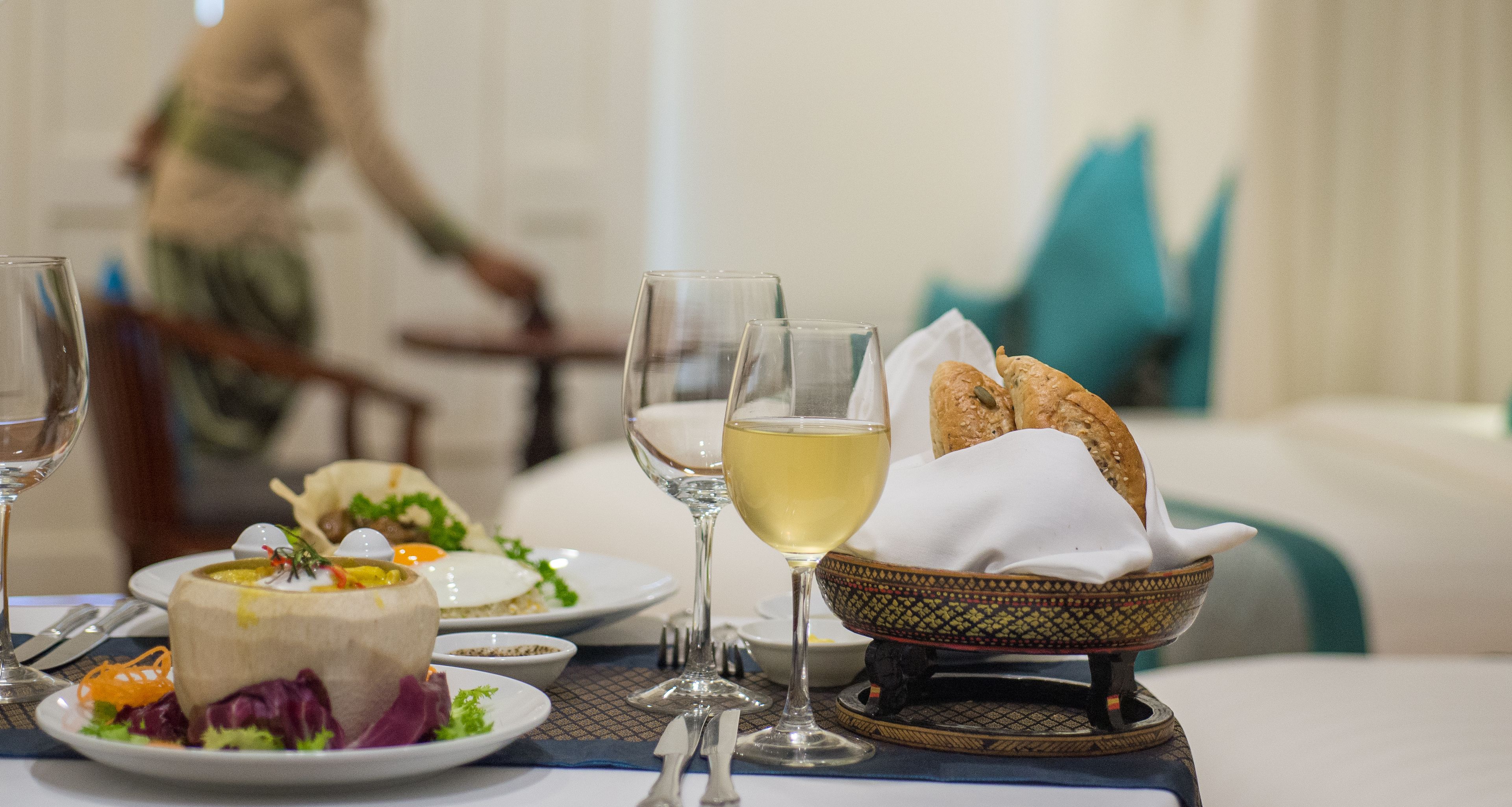 A dining table with plates of food, glasses of wine, and a bowl of bread.