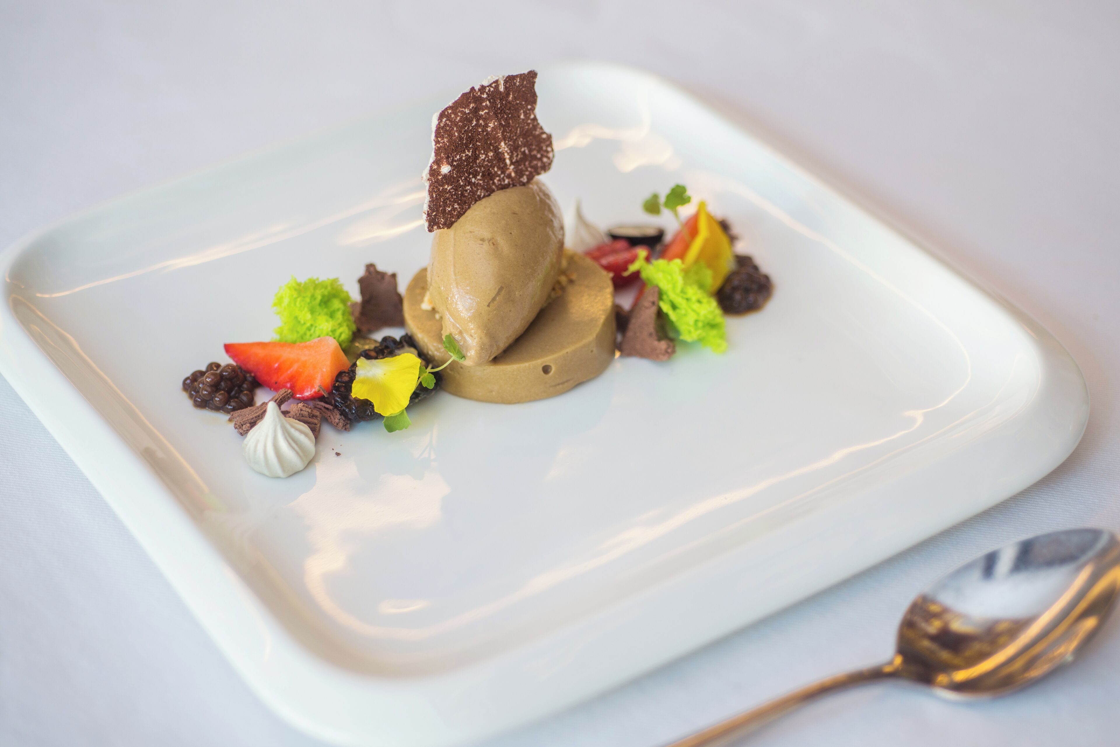 A dessert on a square white plate with a spoon beside it.