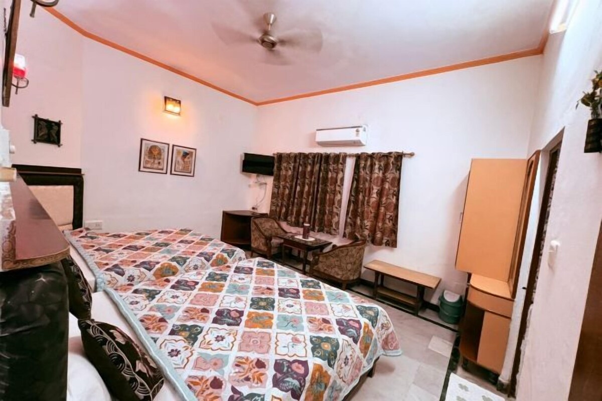 A bedroom with a bed, a desk, a chair, a lamp, an air conditioner, and a ceiling fan.