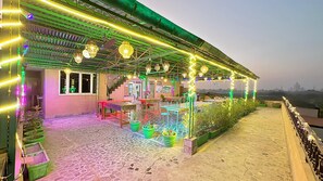 A rooftop terrace with outdoor seating, decorative lights, and a view of a distant landmark. - Hotel Taj Plaza (Agra)