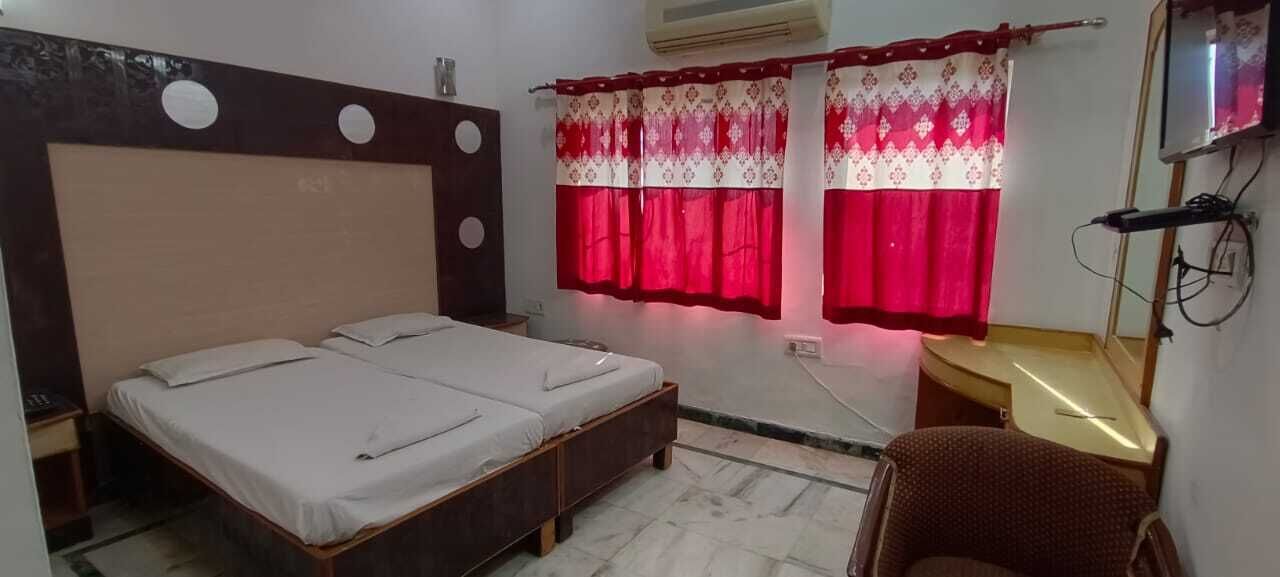 Un dormitorio con cama, escritorio, silla y ventana con cortinas rojas.