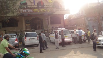 Entrada de hotel con un cartel, acceso mediante portón y vehículos estacionados.