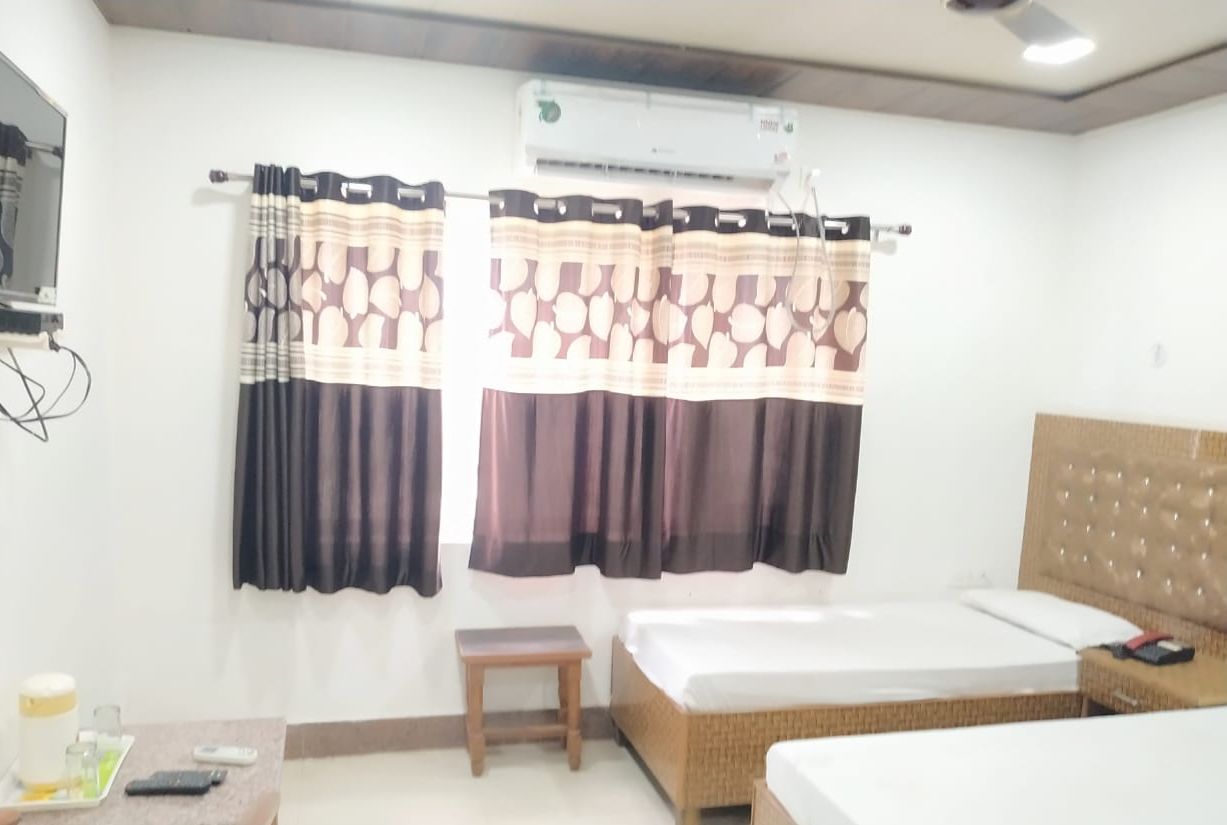 A hotel room with a bed, a small table, a chair, an air conditioning unit, and a curtain with a pattern.