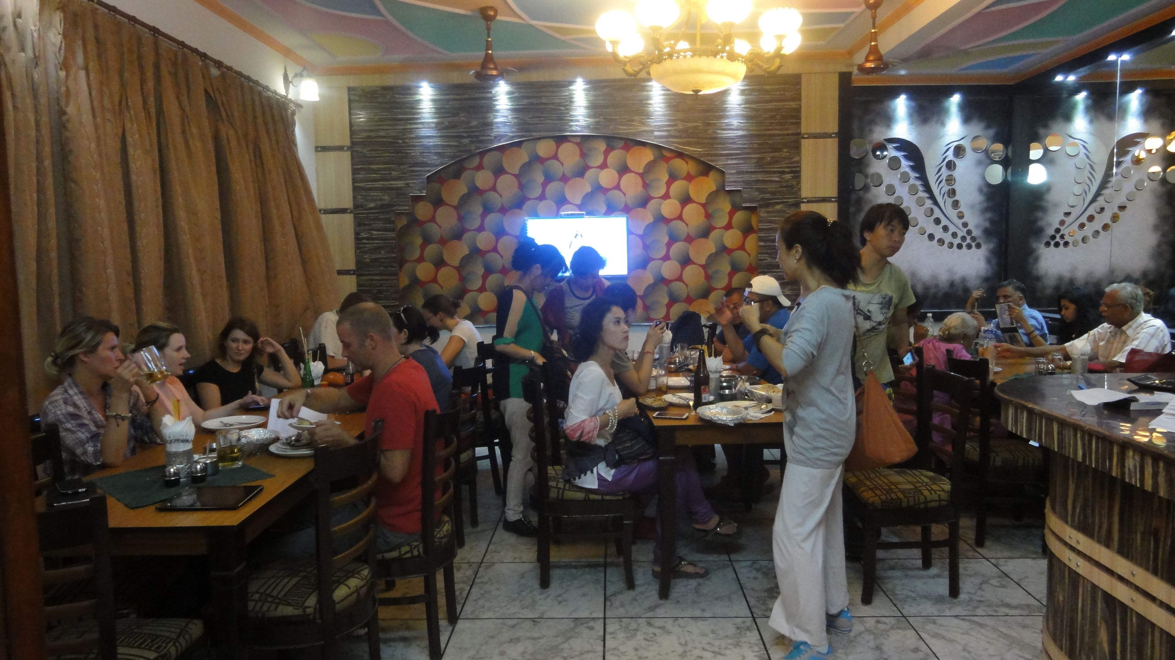 A restaurant with multiple tables and chairs, a decorative wall with circular patterns, and a chandelier.