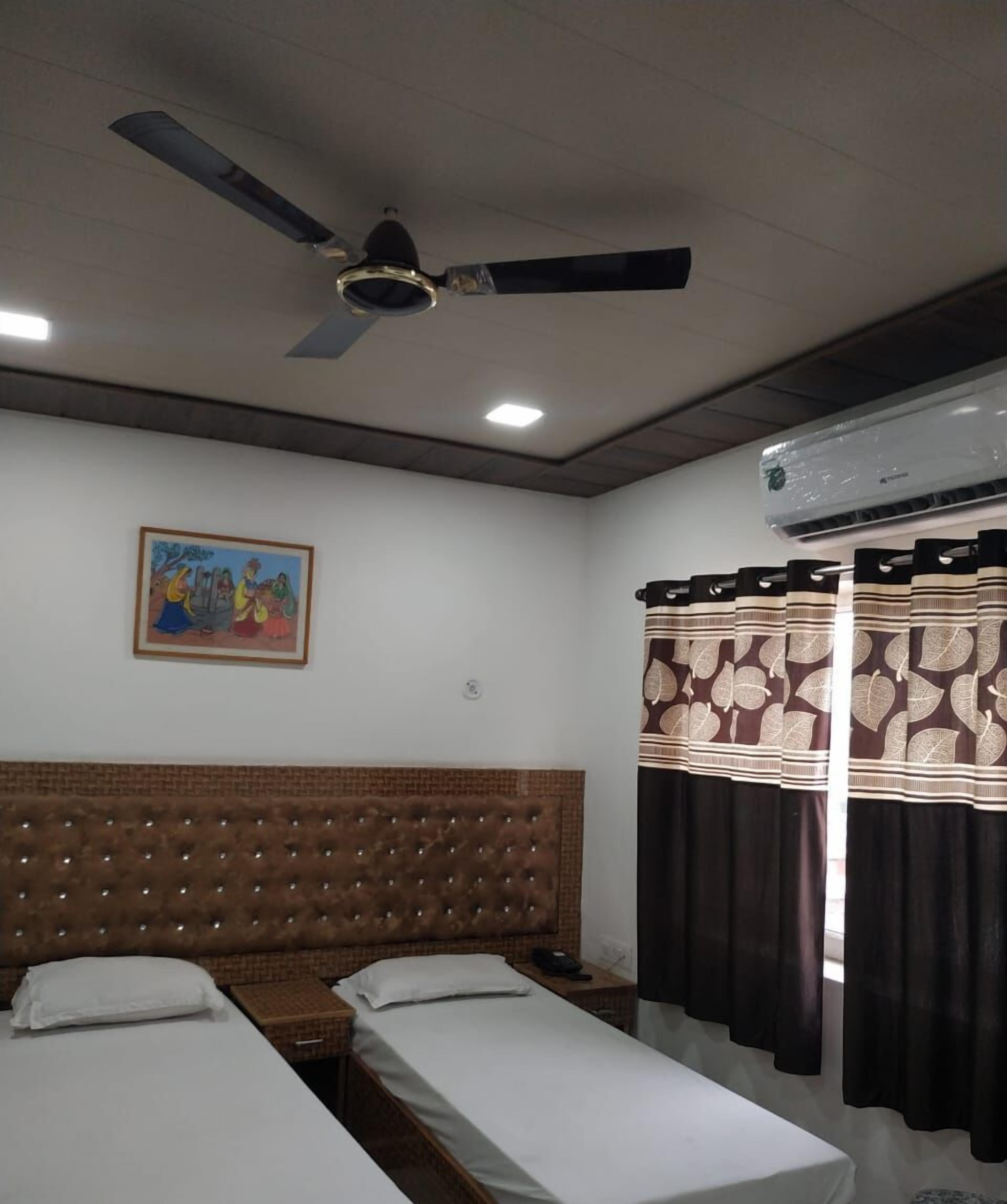 A room with two single beds, a ceiling fan, an air conditioning unit, and a painting on the wall.