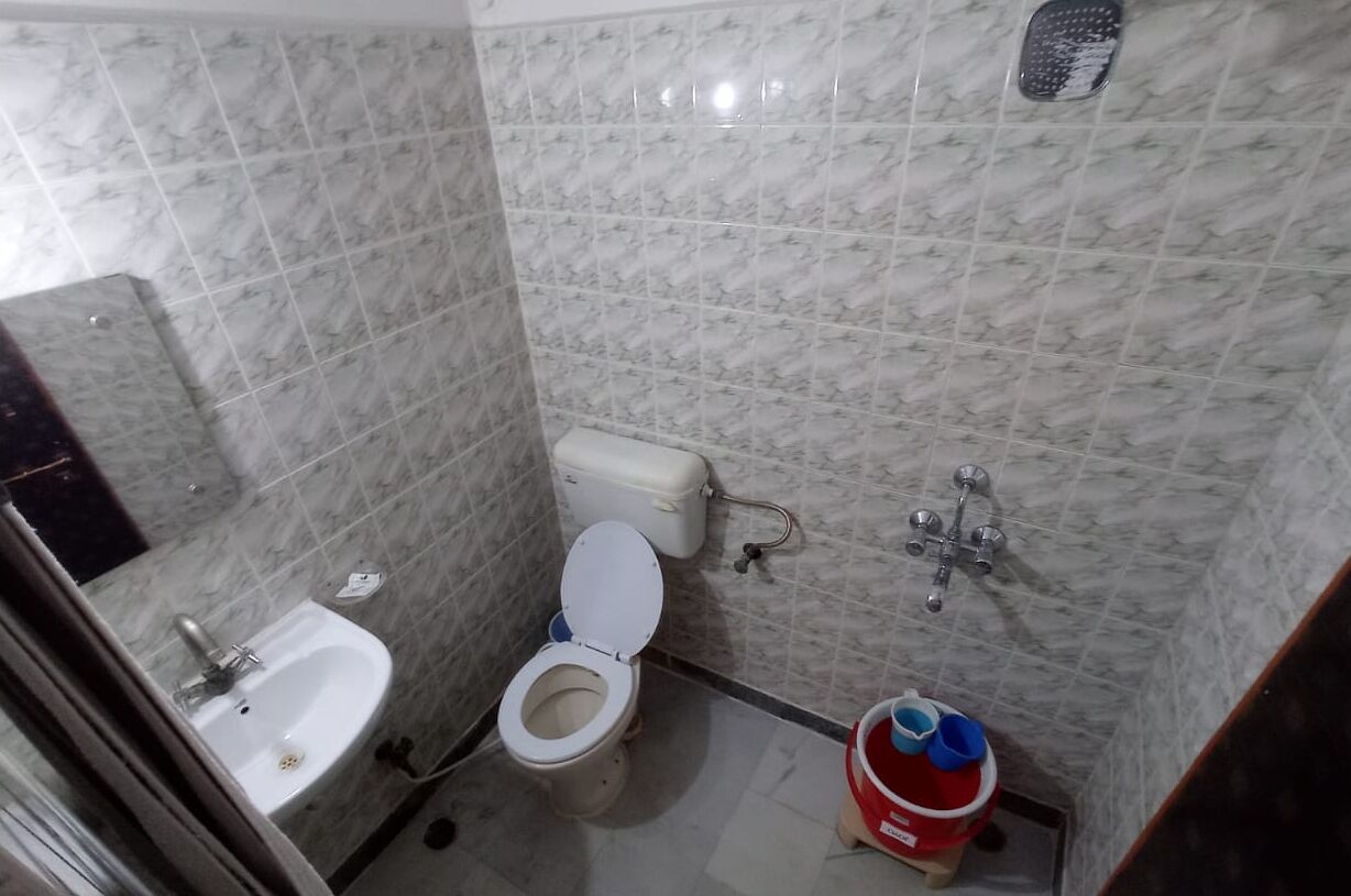 A small bathroom with a toilet, sink, and a red bucket.