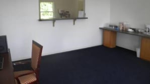 A room with a dark carpet, a wooden chair, a small table, a mirror, and a kitchenette area with cabinets and a countertop. - USA Inn and Suites Morgantown (Morgantown)