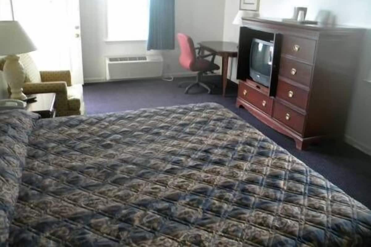 A hotel room with a large bed, a desk with a chair, a television, and a dresser.