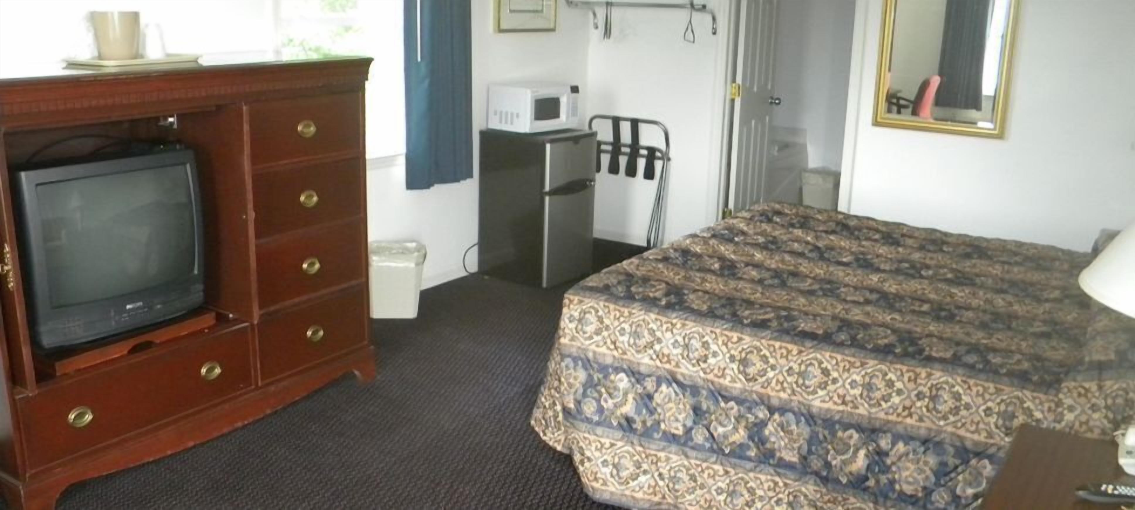 A hotel room with a bed, a wooden dresser with a television, a microwave, and a small desk.