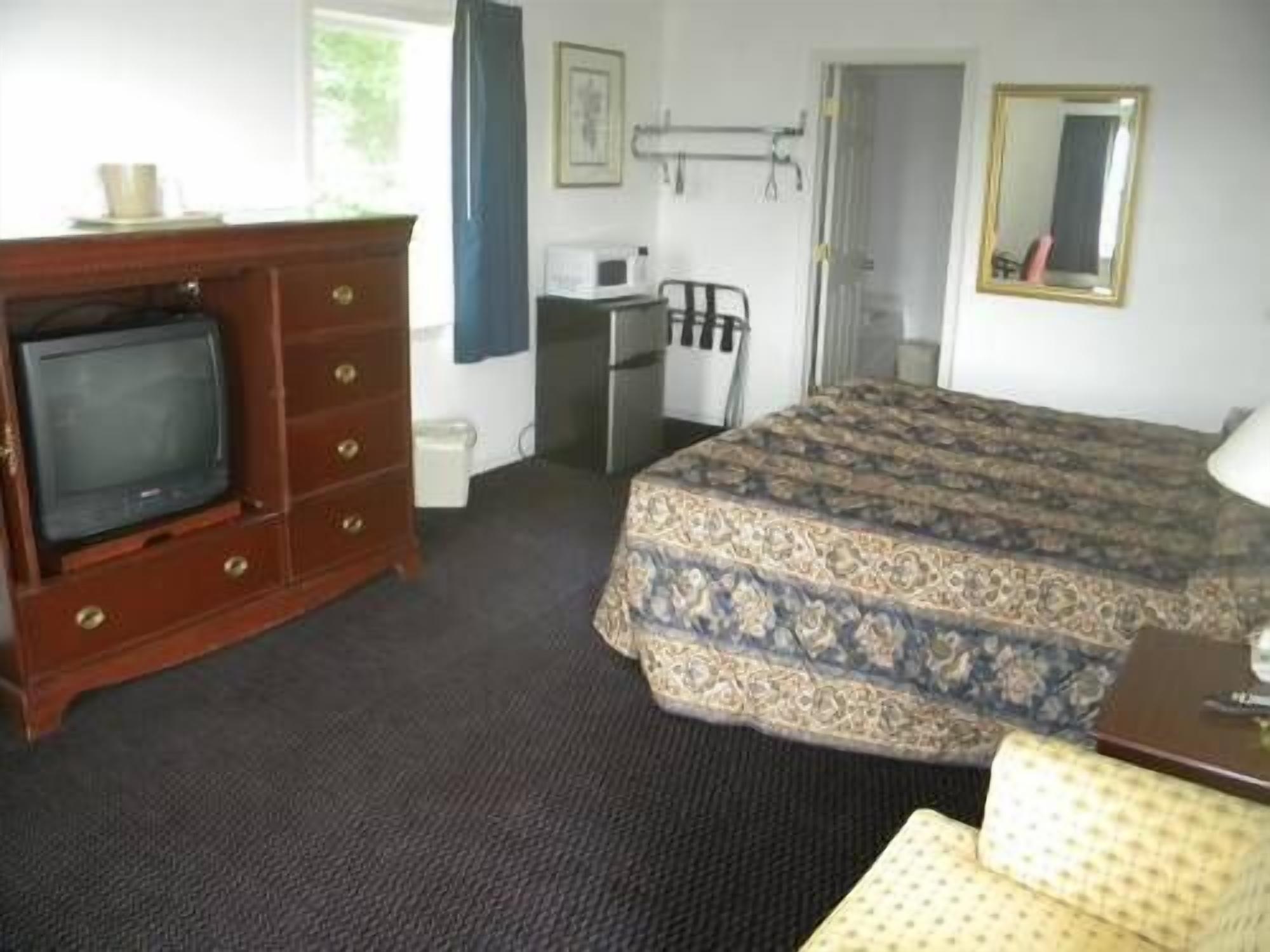 Una habitación de hotel con una cama, televisión, cómoda, silla y una mesita.
