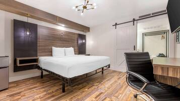 Une chambre à coucher moderne avec un plancher en bois, un lit avec une literie blanche, un fauteuil de bureau noir et un bureau.