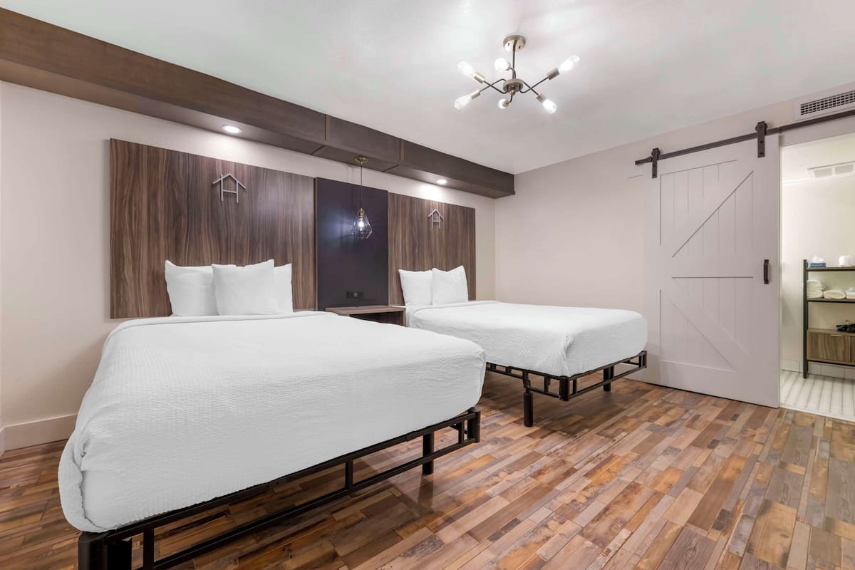 A hotel room with two beds, wooden flooring, a modern chandelier, and a sliding door closet.