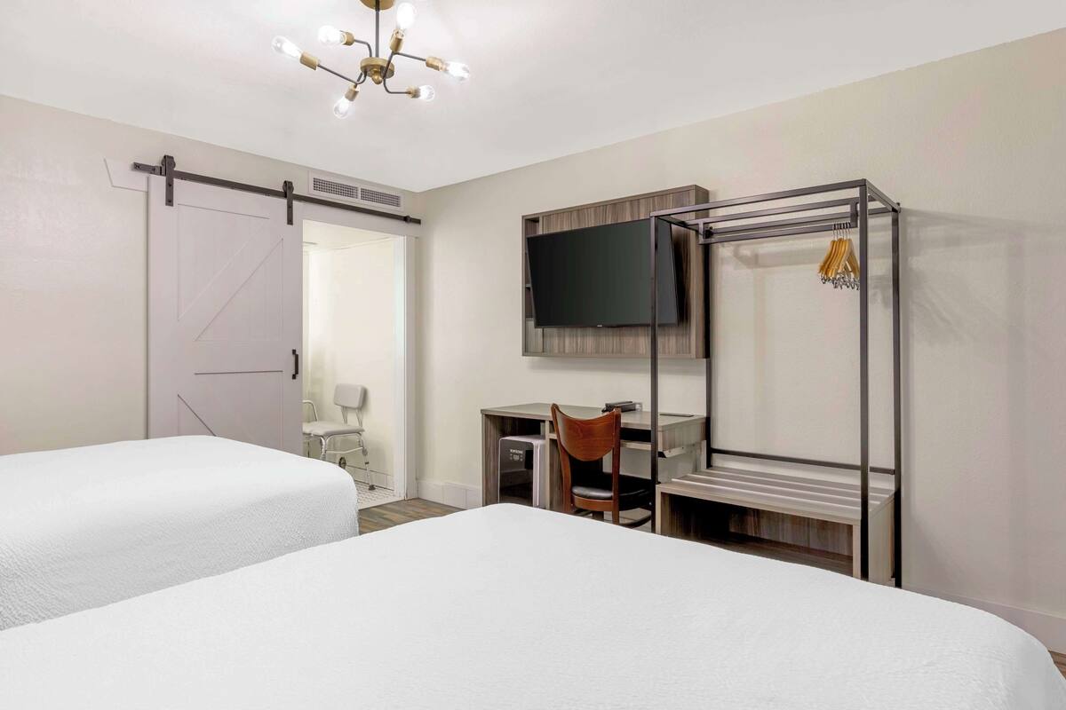 A hotel room with two beds, a desk, a chair, a TV, and a wardrobe.