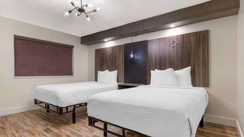 A hotel room with two single beds, a wooden floor, a large window, and a modern chandelier.