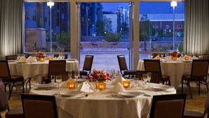 A dining area with tables set for a meal, large windows offering a view of the cityscape, and warm lighting.