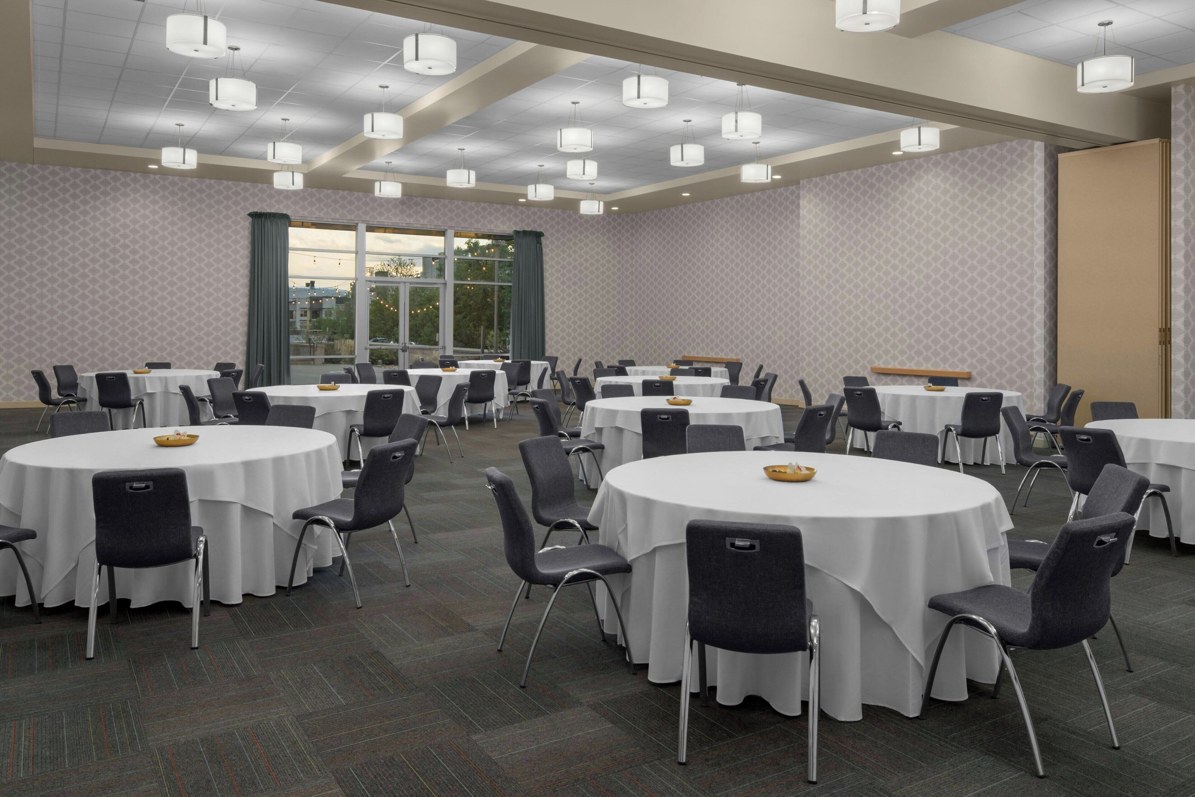 A conference room with multiple round tables and chairs, large windows, and a patterned wall.