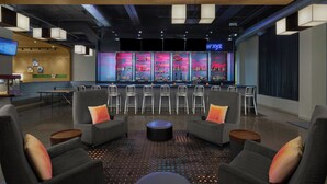 A modern bar area with a bar counter, seating with round ottomans, and a neon sign.
