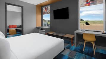 A modern hotel room with a large bed, a desk, a chair, and a window with a view of the beach.