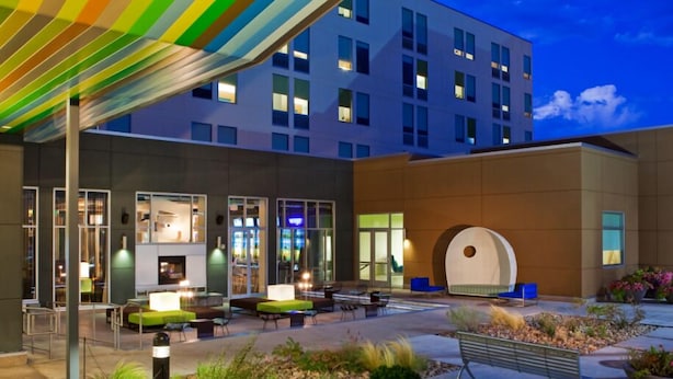 A modern hotel with a covered outdoor seating area, large windows, and a well-lit interior.