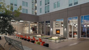 A modern outdoor seating area with tables and chairs, a fireplace, and a glass-enclosed reading area.