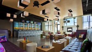 A modern lounge area with leather sofas, wooden tables, and a bar with a colorful mural.
