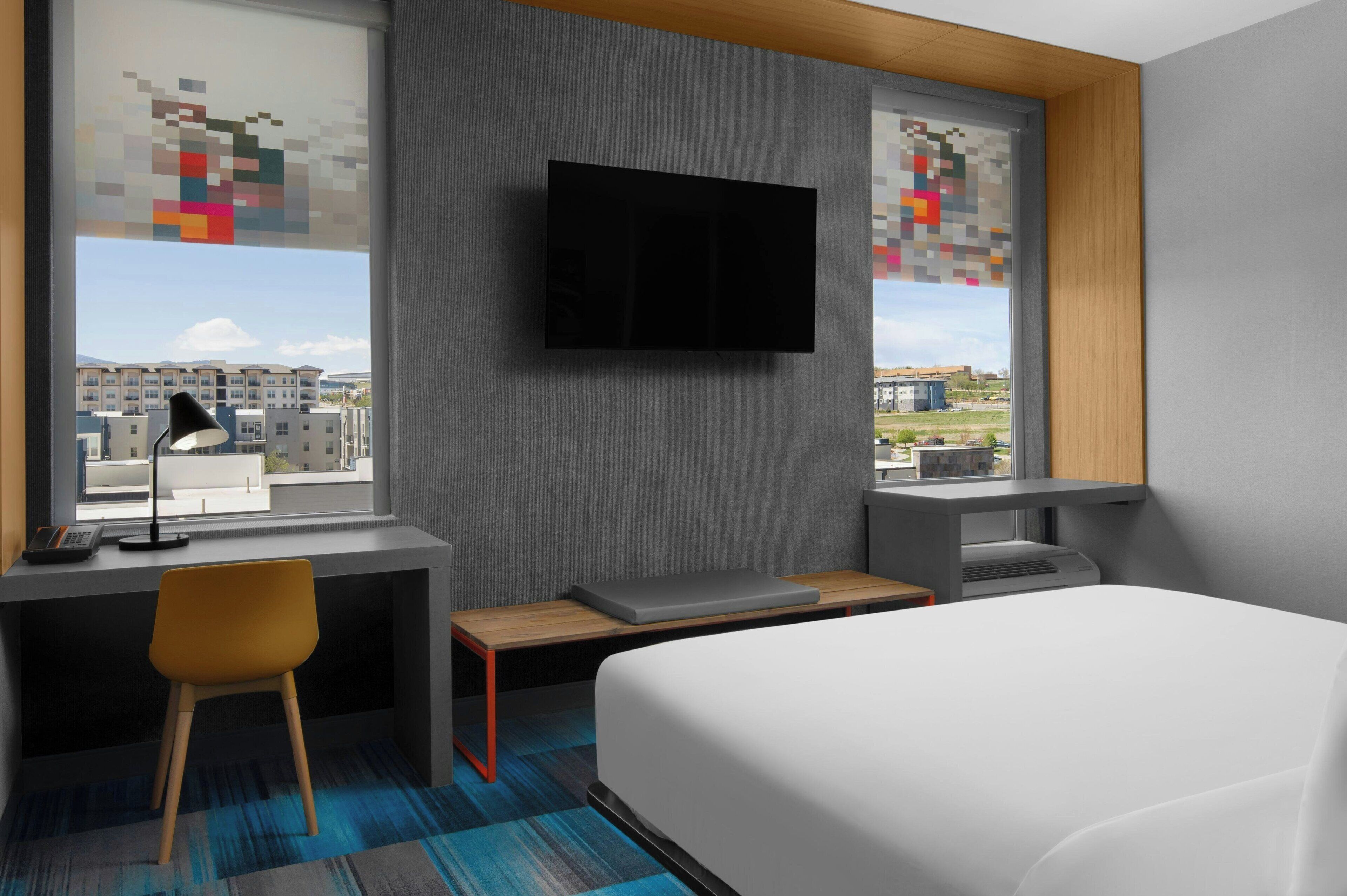 Une chambre d’hôtel moderne équipée d’un lit, d’un bureau, d’une chaise et d’un téléviseur.