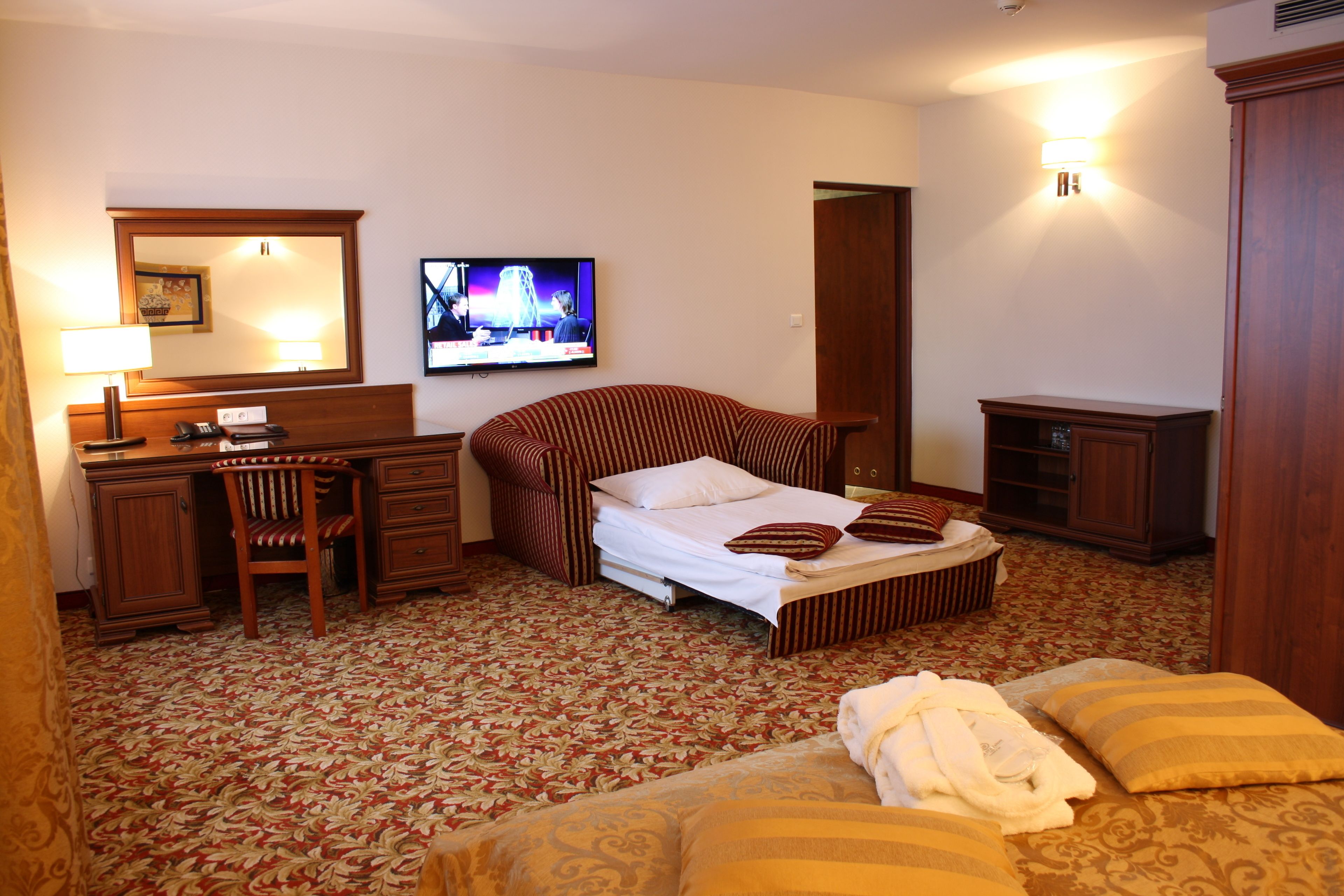 A hotel room with a bed, a desk, a chair, a television, and a wardrobe.