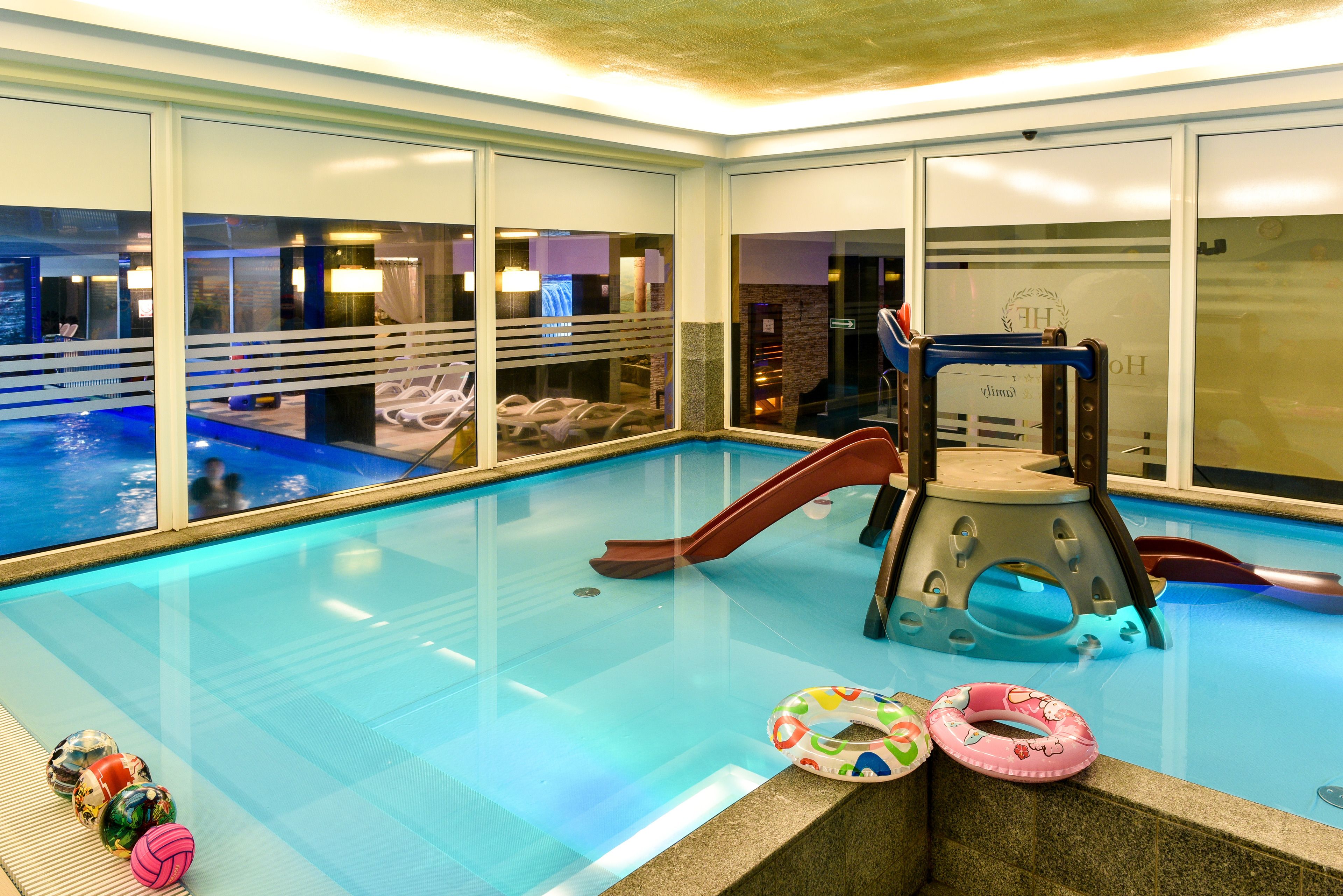 Una piscina interior amb tobogan, gandules i vistes a la ciutat a través de grans finestres.