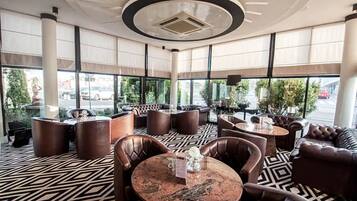 A modern indoor seating area with leather furniture, patterned flooring, and large windows offering a view of the street.