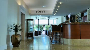 Un vestíbulo con un letrero que dice claramente “LOBBY”, una recepción, una planta grande en maceta y una zona de estar con sillas y un sofá.
