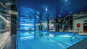 Una piscina interior con agua cristalina, una silla de salvavidas y una zona junto a la piscina con sillones de descanso.