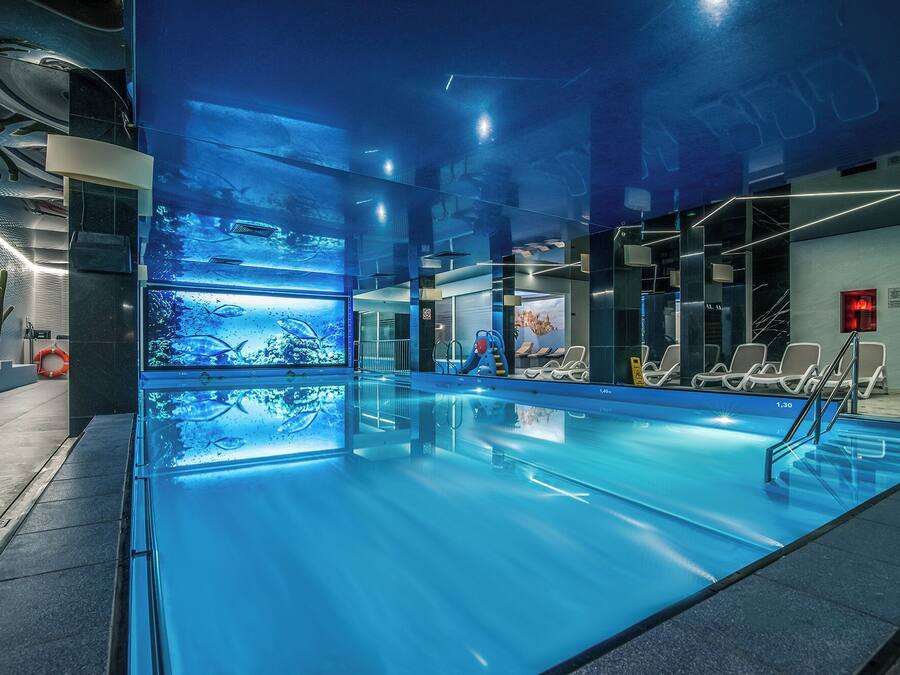 An indoor swimming pool with clear water, a lifeguard chair, and a poolside area with lounge chairs.