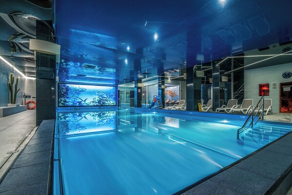 An indoor swimming pool with clear water, a lifeguard chair, and a poolside area with lounge chairs. - Hotel SPA Faltom Gdynia Rumia (Rumia)